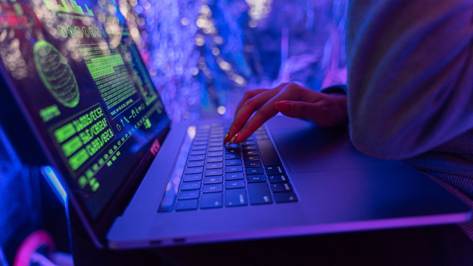 A person typing on a laptop showing data panels, in purple light