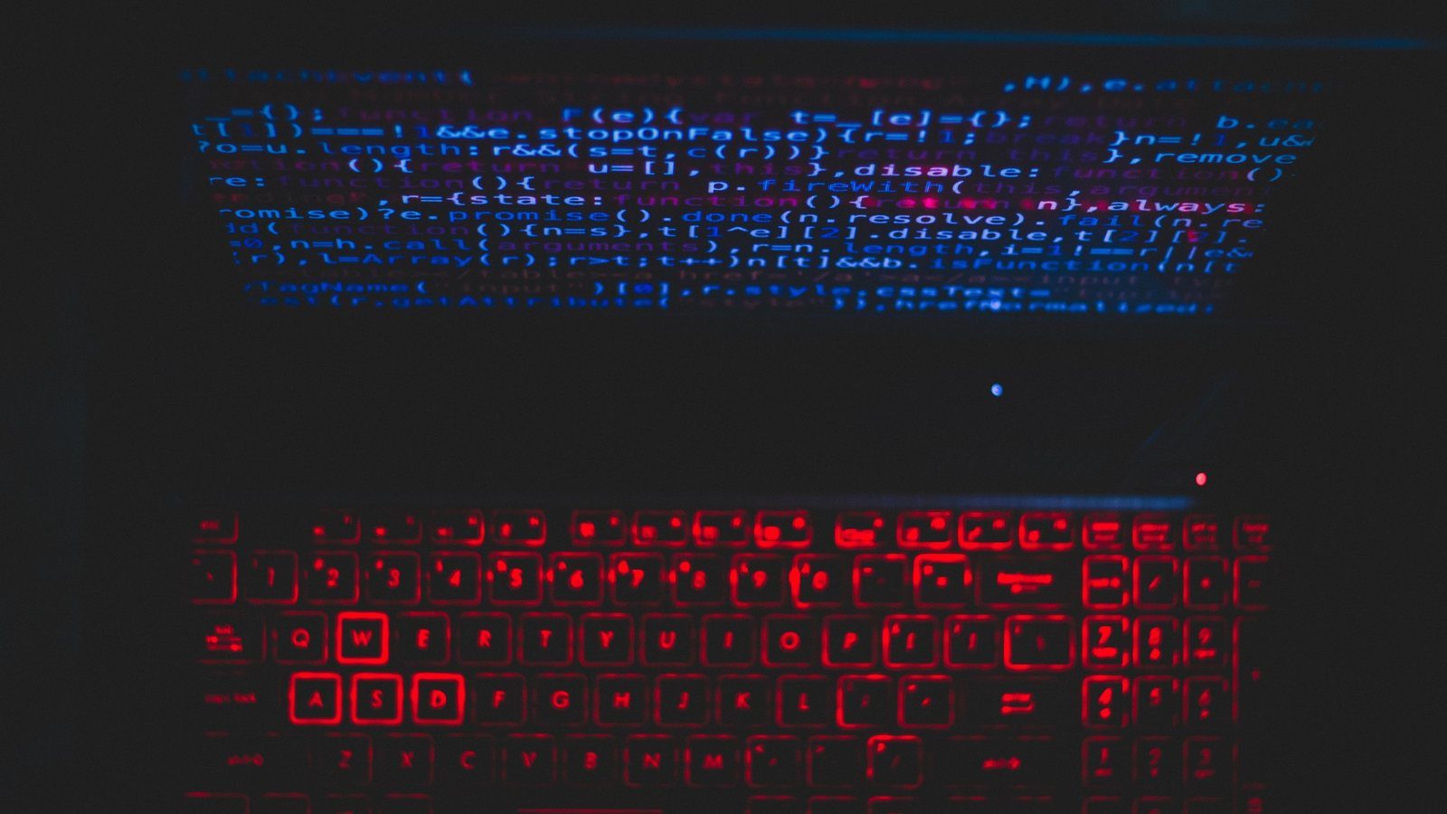 A laptop with a red-backlit keyboard and code reflected on its screen